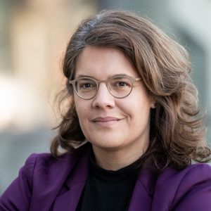 Porträt von Prof. Dr. Sina Farzin, die einen lila Blazer und ein schwarzes Oberteil trägt. Sie trägt Brille und hat braunes, schulterlanges, gelocktes Haar. Sie lächelt leicht mit geschlossenem Mund. 